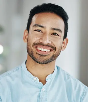 Smiling man with healthy teeth in light blue shirt at Mineola dental practice.