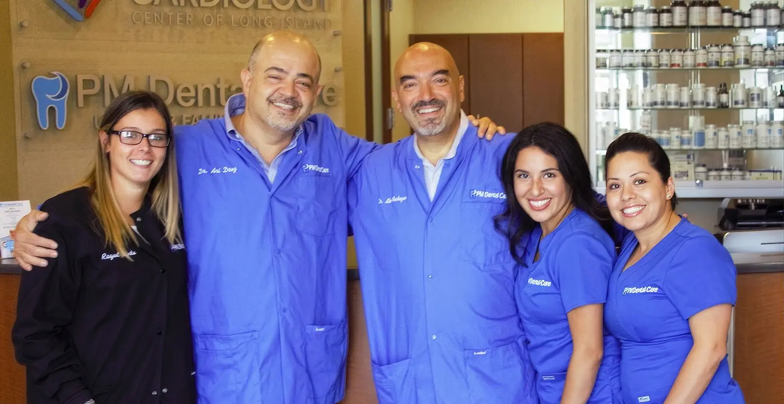 Friendly dental team in blue scrubs smiling together in Mineola dental office.