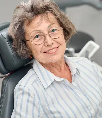 Smiling older woman wearing glasses in dental chair during sedation dentistry treatment.
